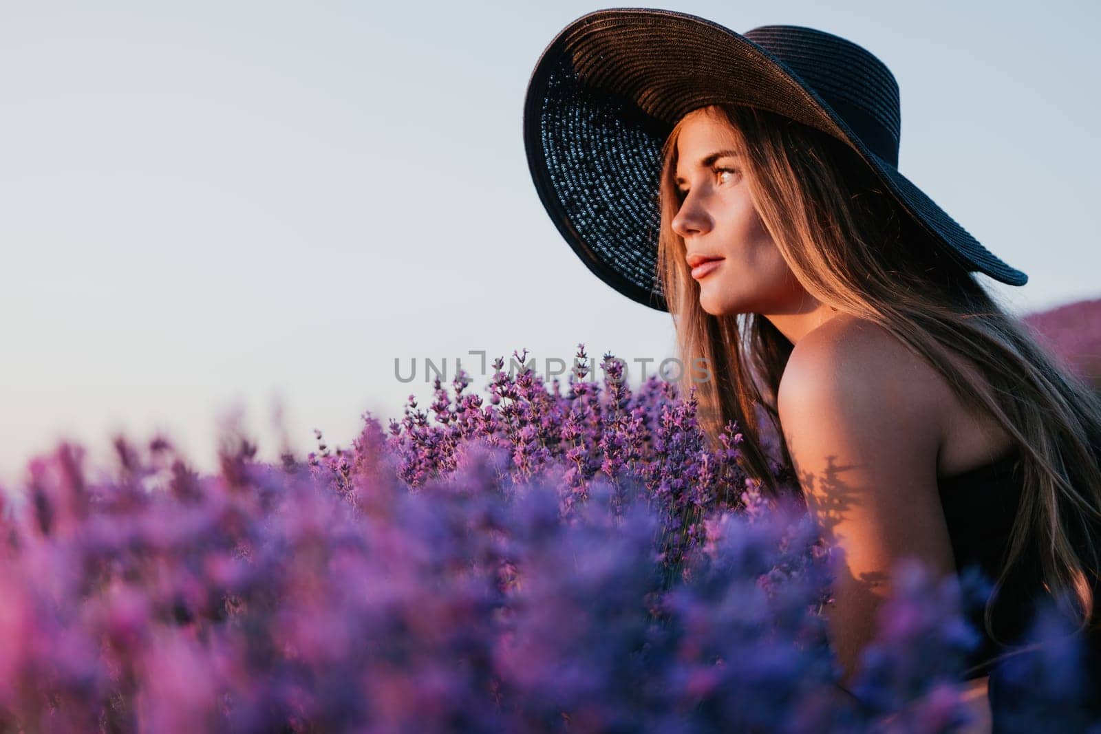 Close up portrait of young beautiful woman in a white dress and a hat is walking in the lavender field and smelling lavender bouquet.