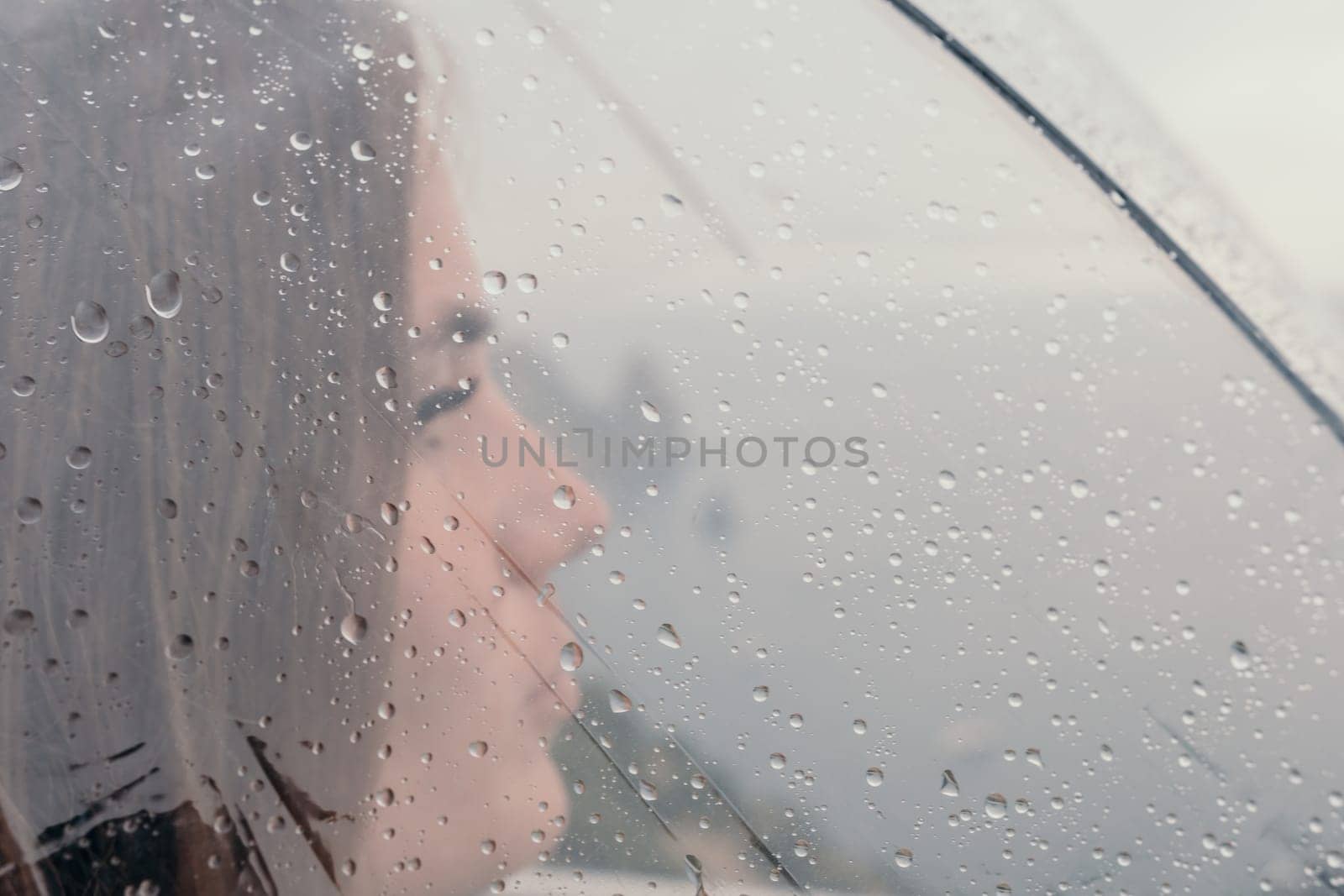 Woman rain umbrella. Happy woman portrait wearing a raincoat with transparent umbrella outdoors on rainy day in park near sea. Girl on the nature on rainy overcast day. by panophotograph