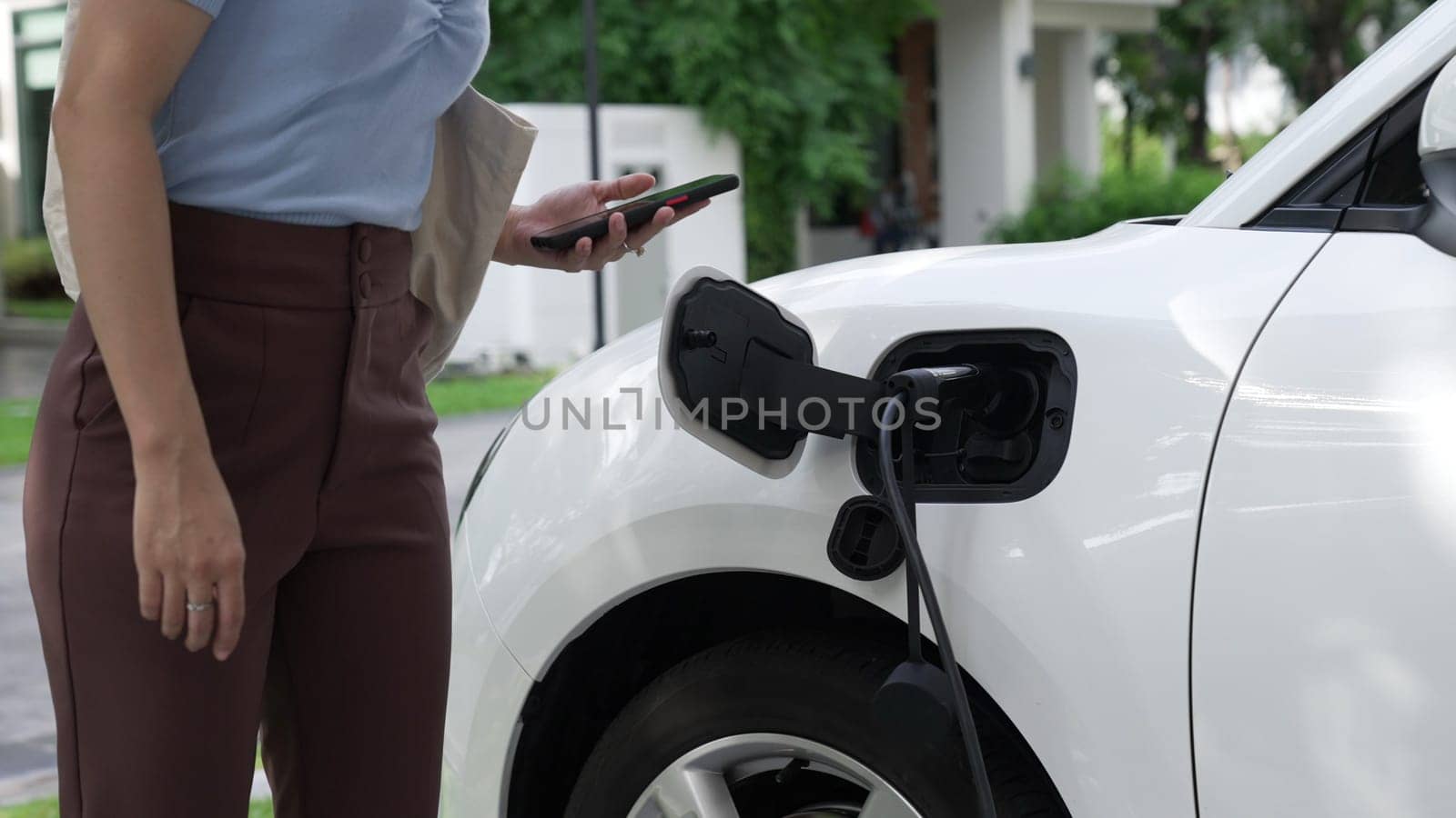 Progressive lifestyle of a modern woman who have just returned from work in an electric vehicle that is being charged at home. Electric vehicle powered by sustainable clean energy.