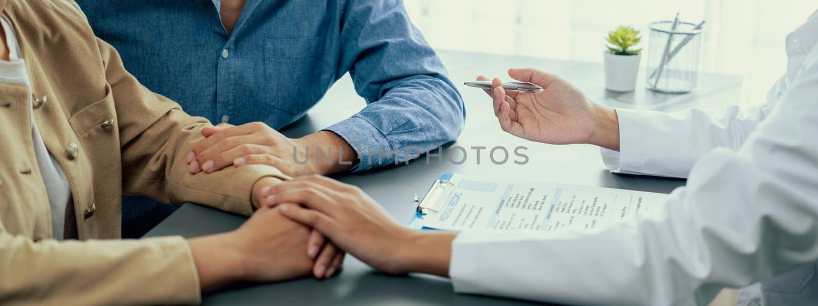 Doctor providing compassionate healthcare consultation while young couple patient holding hand, comfort each other after infertile report. Reproductive and medical fertility consulting. Neoteric