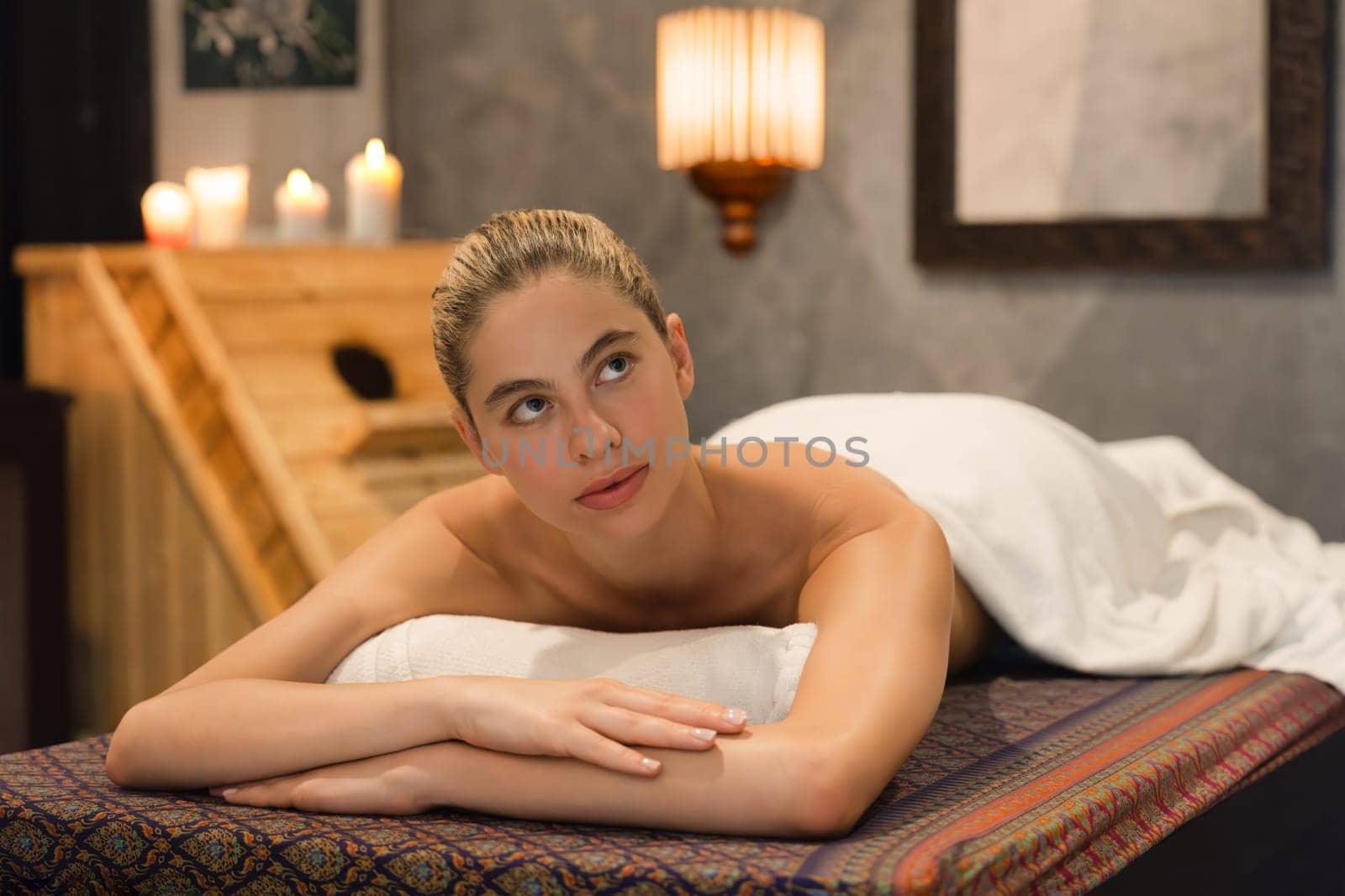 Portrait of beautiful caucasian woman in white towel woman lies on spa bed in front of warm wooden sauna cabinet with relaxation and peaceful at spa salon. Close up. A Side view. Tranquility.