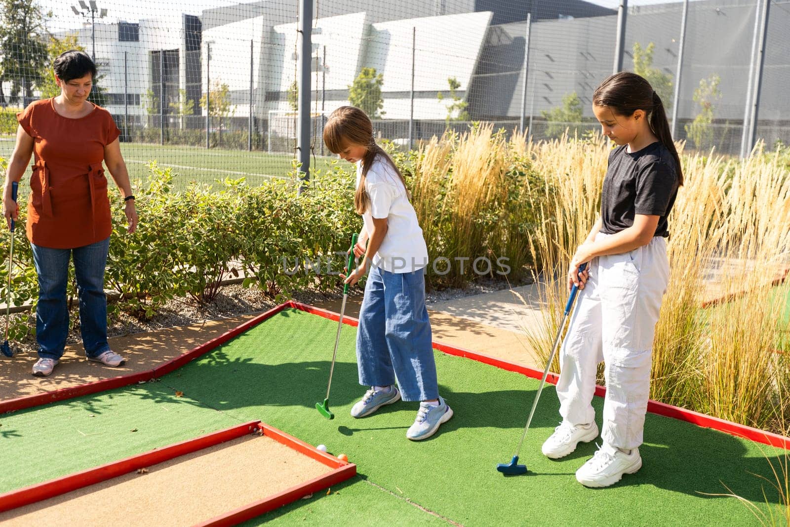 Cute school girl playing mini golf with family. Happy toddler child having fun with outdoor activity. Summer sport for children and adults, outdoors. Family vacations or resort. High quality photo