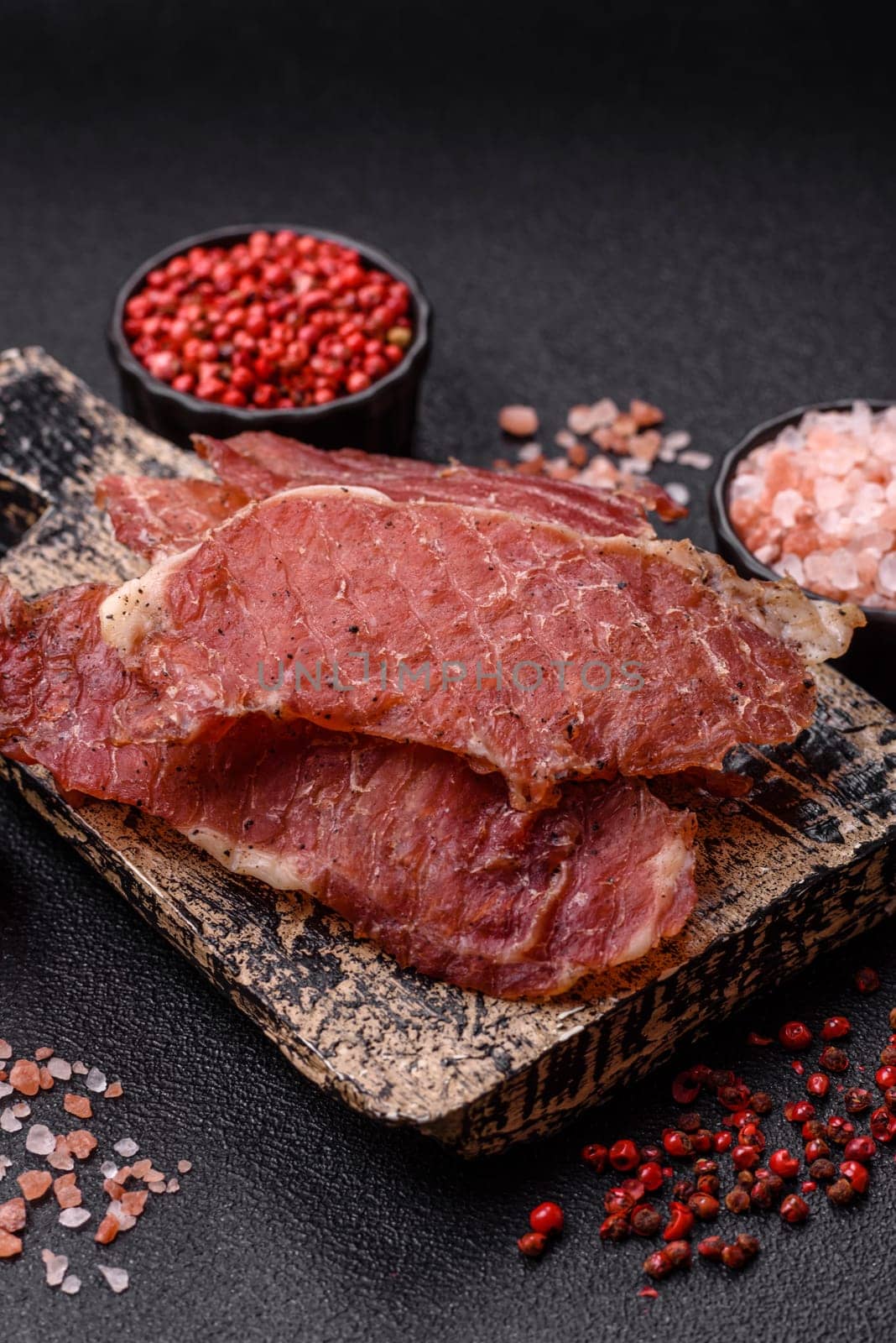 Jerky, dried pork meat slices with salt and spices on a dark concrete background