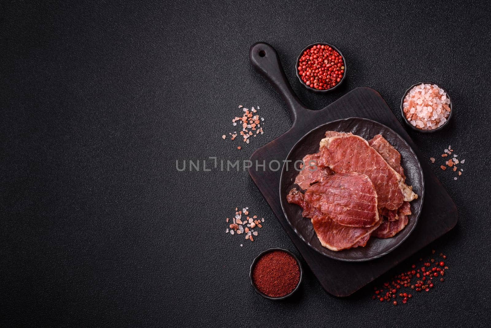 Jerky, dried pork meat slices with salt and spices on a dark concrete background
