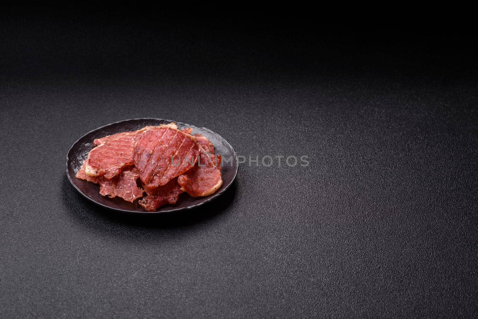 Jerky, dried pork meat slices with salt and spices on a dark concrete background