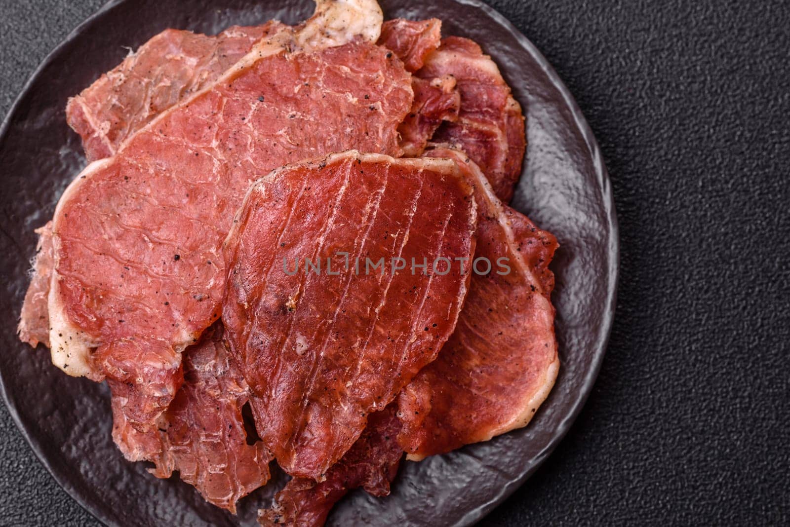 Jerky, dried pork meat slices with salt and spices on a dark concrete background
