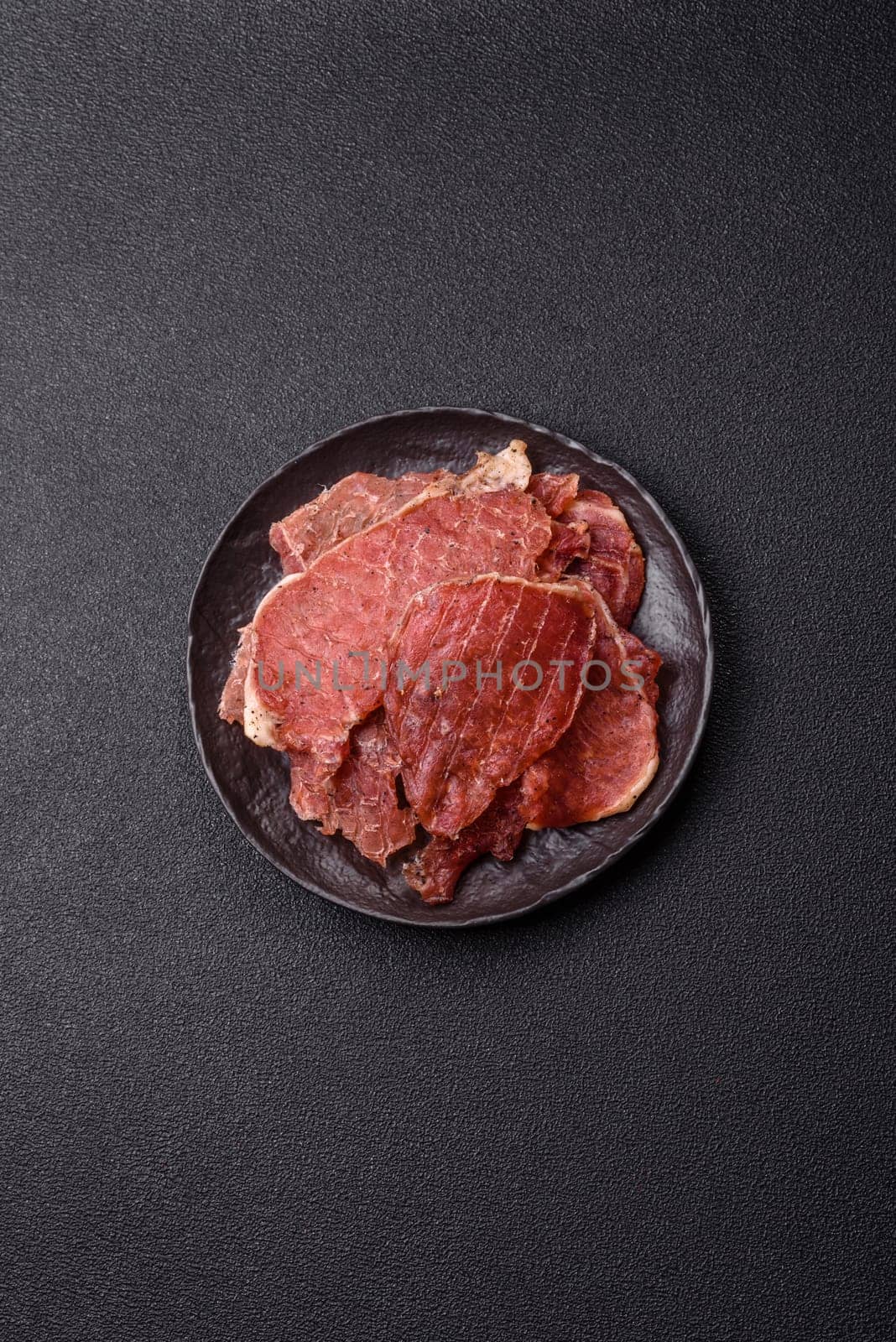 Jerky, dried pork meat slices with salt and spices on a dark concrete background