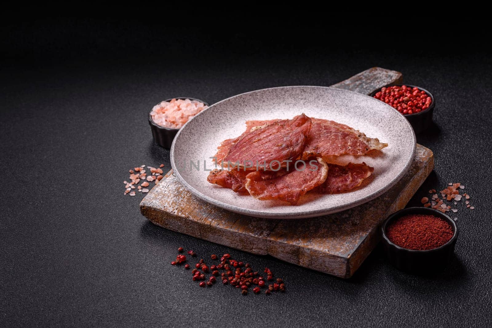 Jerky, dried pork meat slices with salt and spices on a dark concrete background