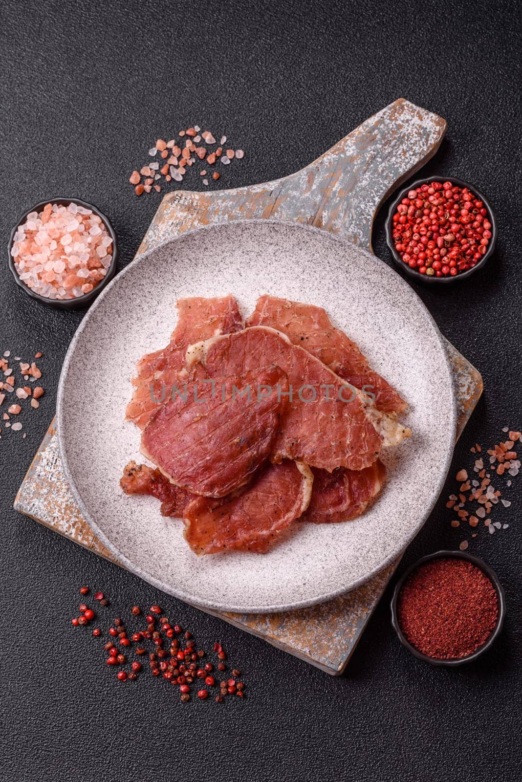 Jerky, dried pork meat slices with salt and spices on a dark concrete background