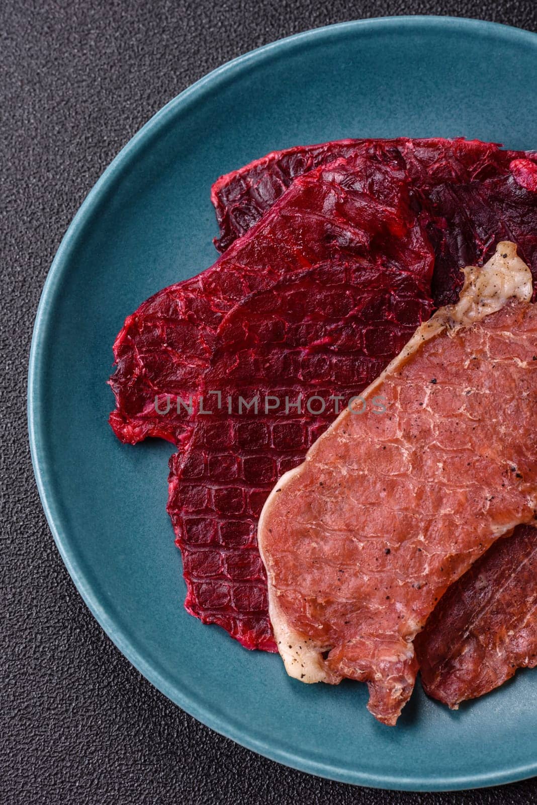 Jerky, dried pork meat slices with salt and spices on a dark concrete background