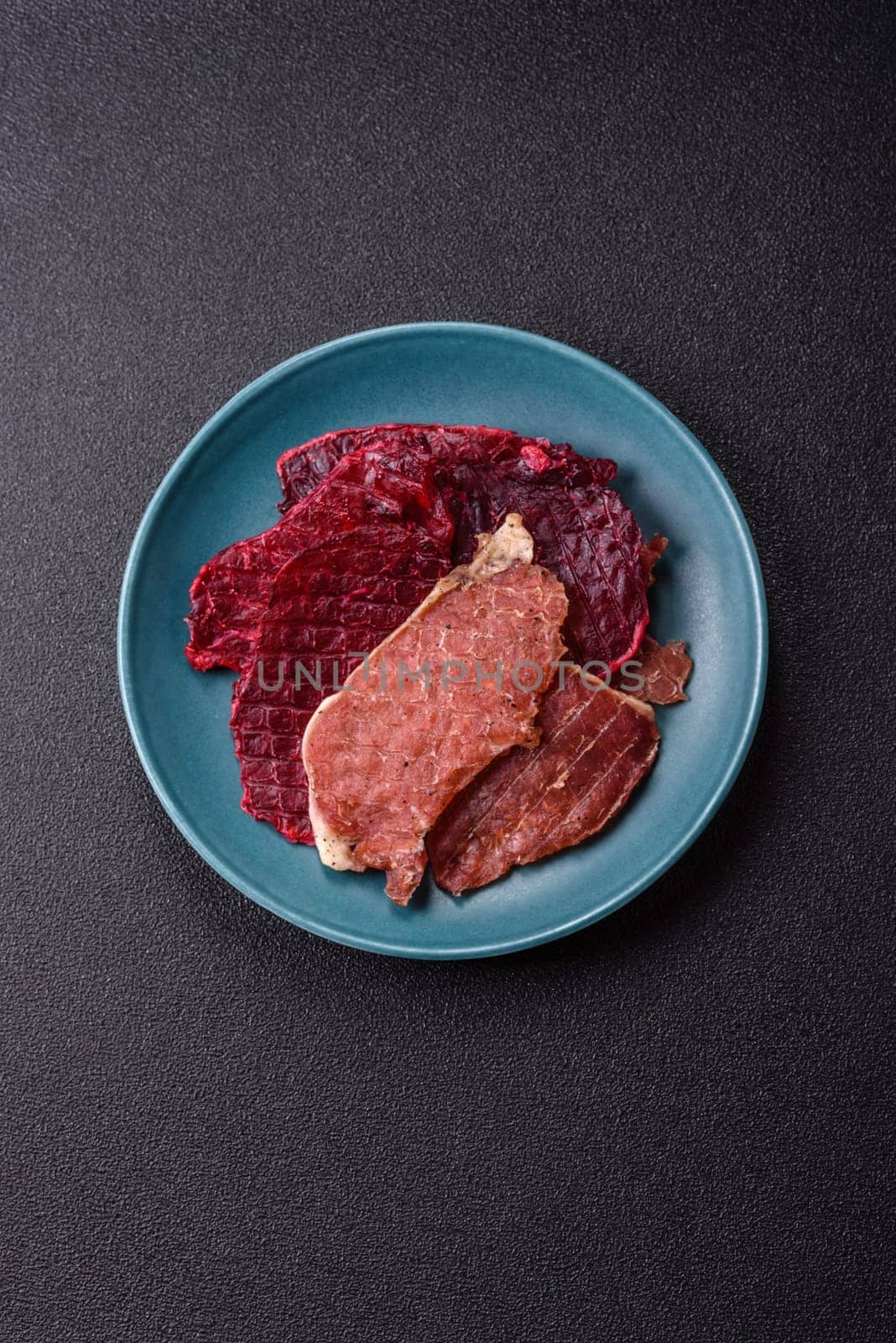 Jerky, dried pork meat slices with salt and spices on a dark concrete background