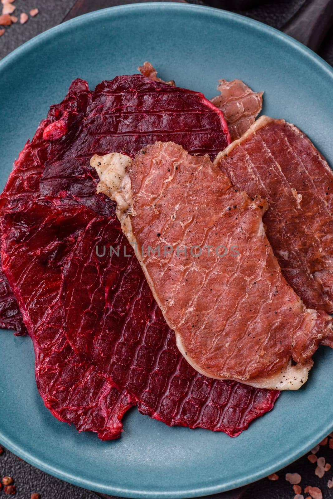 Jerky, dried pork meat slices with salt and spices on a dark concrete background