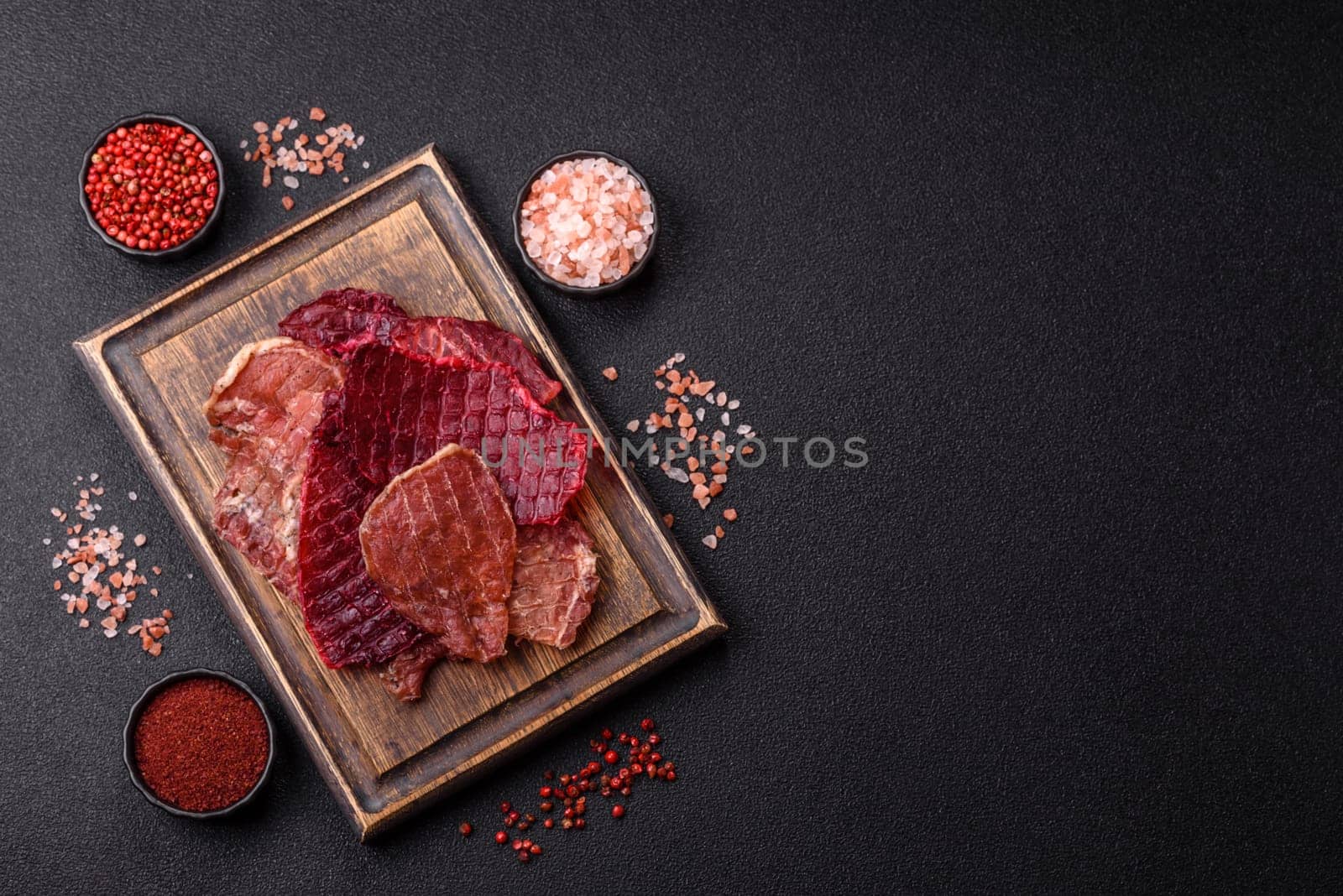 Jerky, dried pork meat slices with salt and spices on a dark concrete background