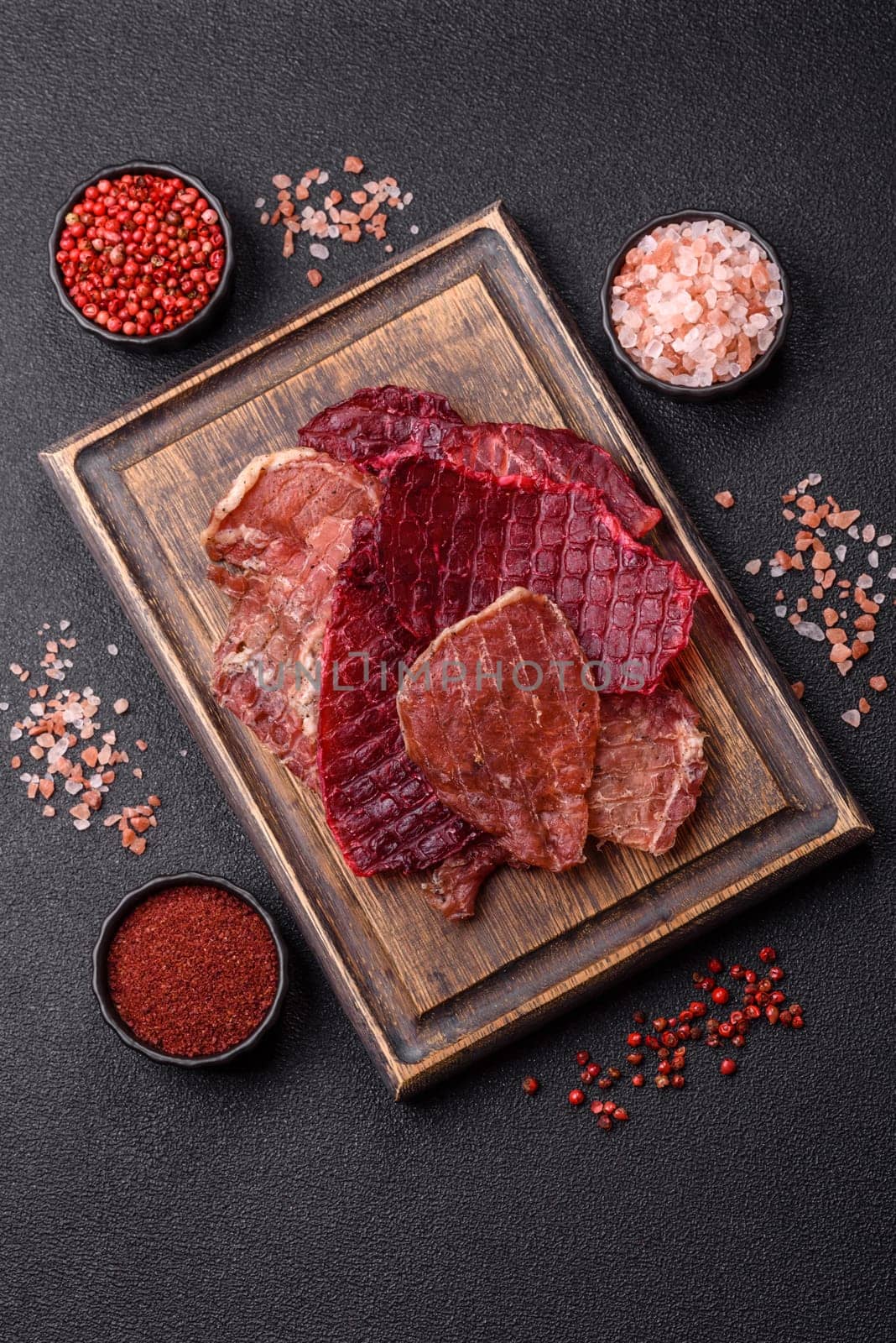 Jerky, dried pork meat slices with salt and spices on a dark concrete background