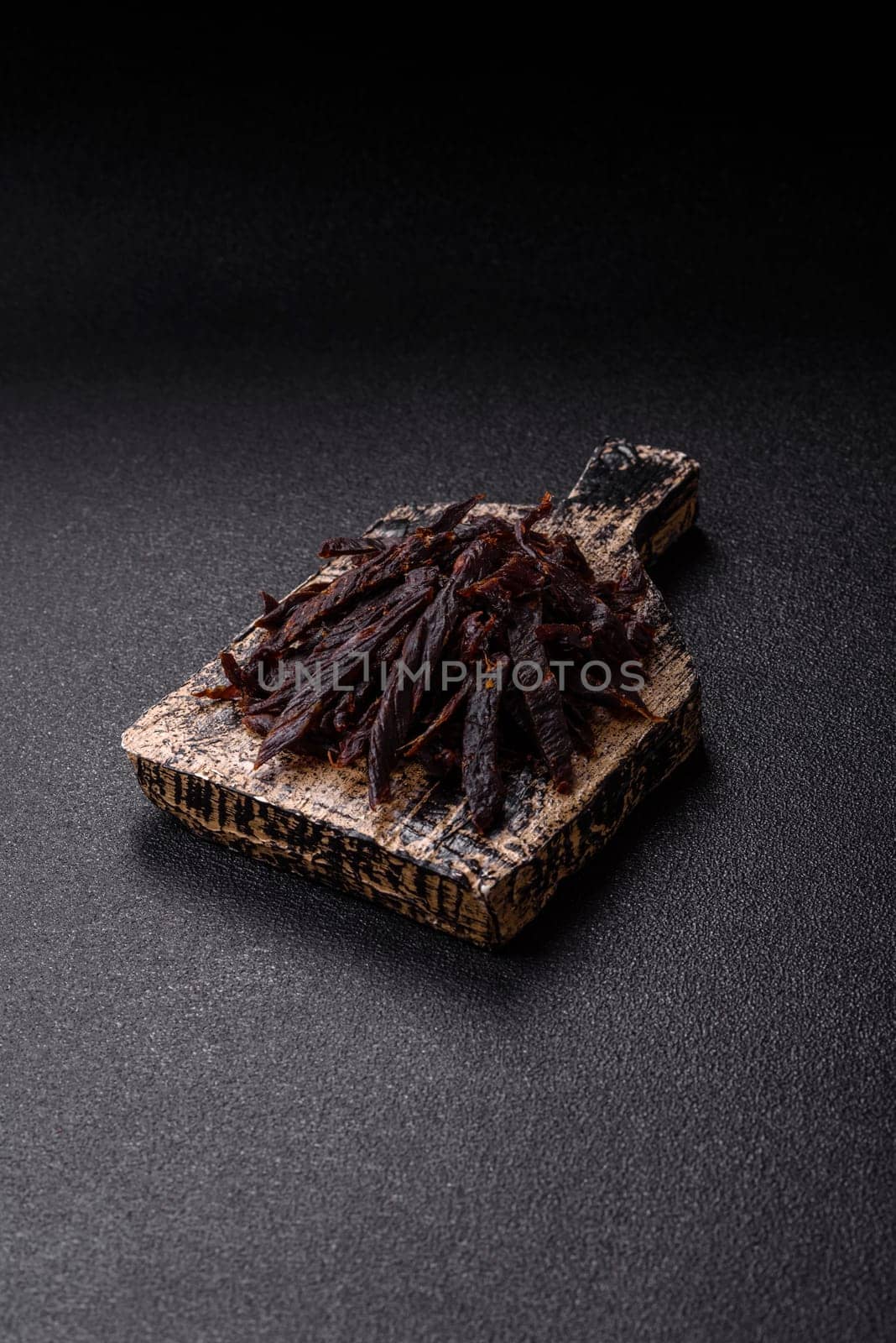 Jerky, dried horse meat or beef slices with salt and spices on a dark concrete background