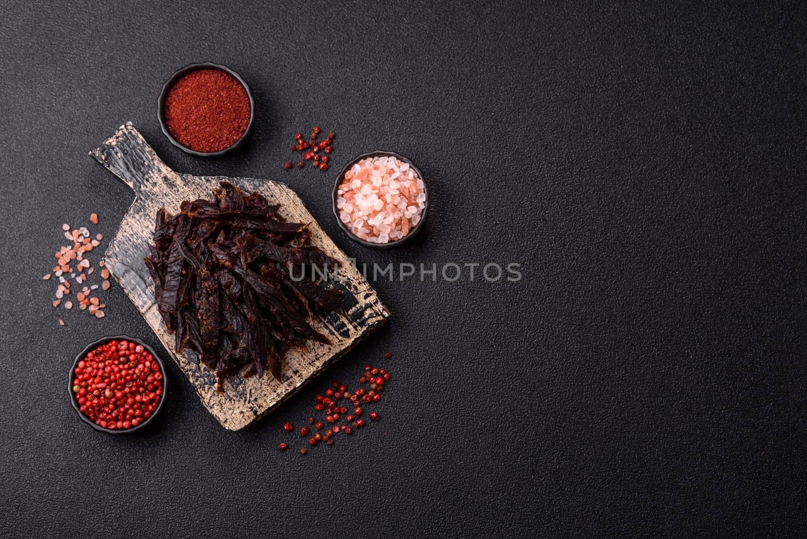 Jerky, dried horse meat or beef slices with salt and spices on a dark concrete background