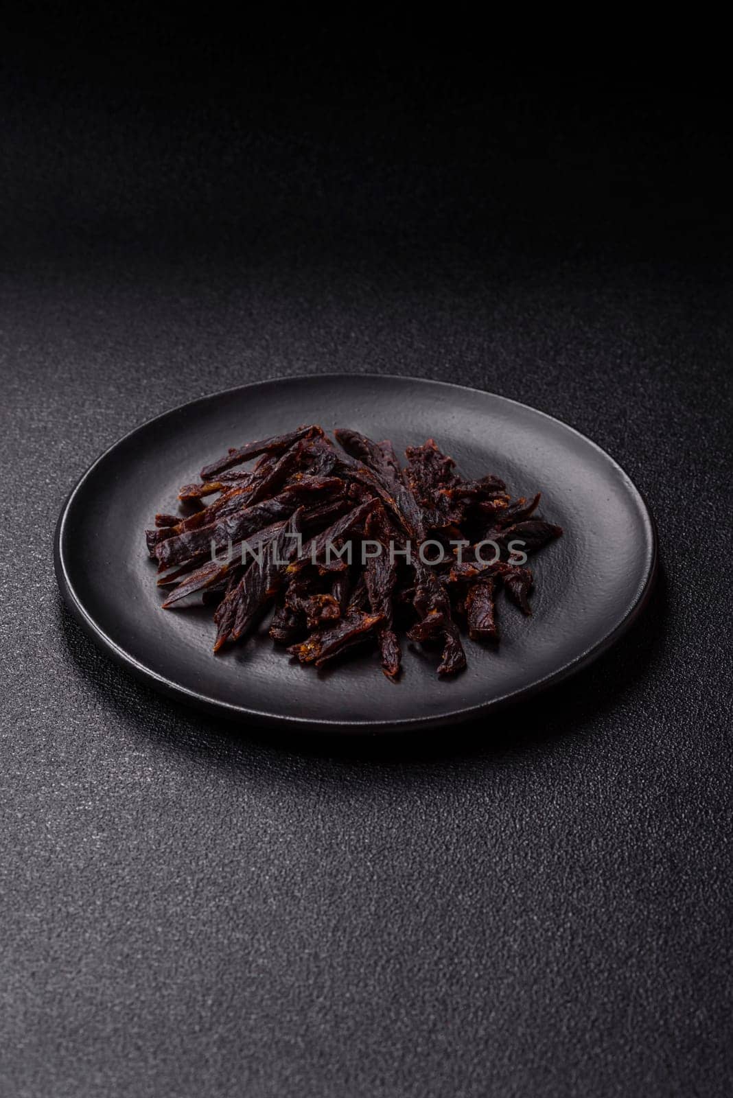 Jerky, dried horse meat or beef slices with salt and spices on a dark concrete background