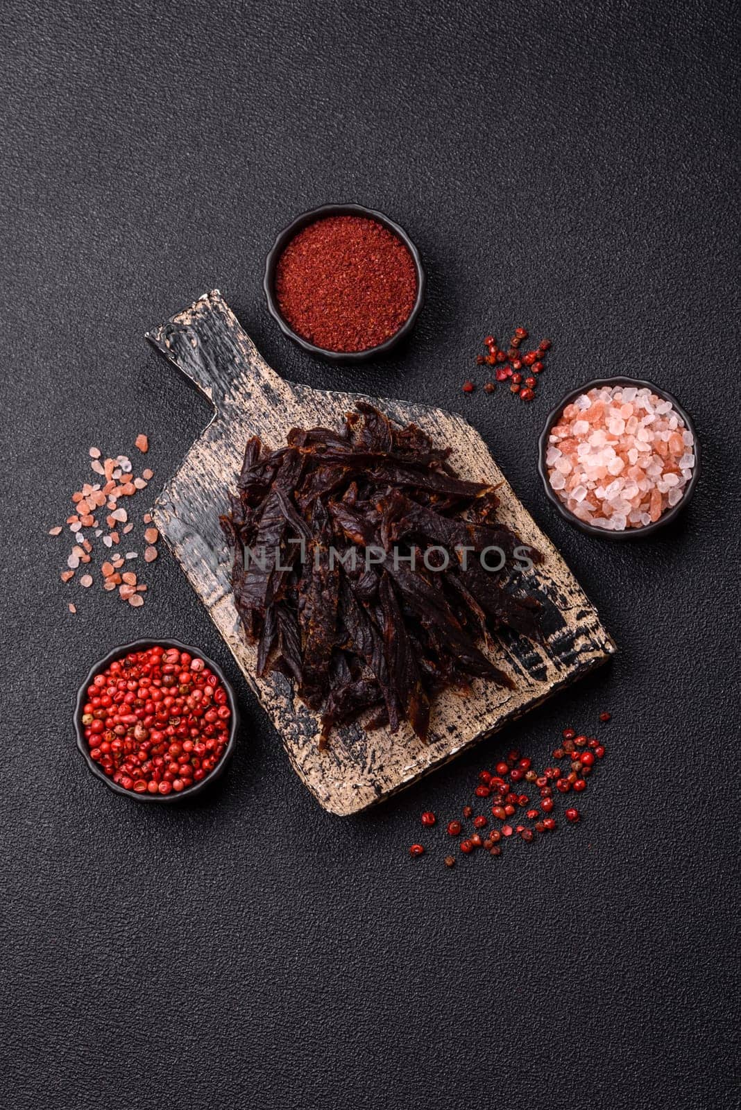 Jerky, dried horse meat or beef slices with salt and spices on a dark concrete background