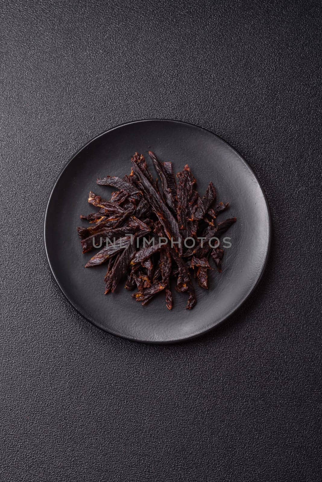 Jerky, dried horse meat or beef slices with salt and spices on a dark concrete background