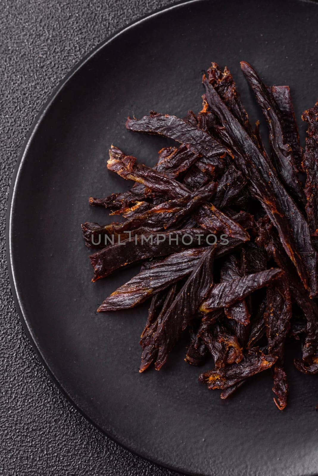 Jerky, dried horse meat or beef slices with salt and spices on a dark concrete background