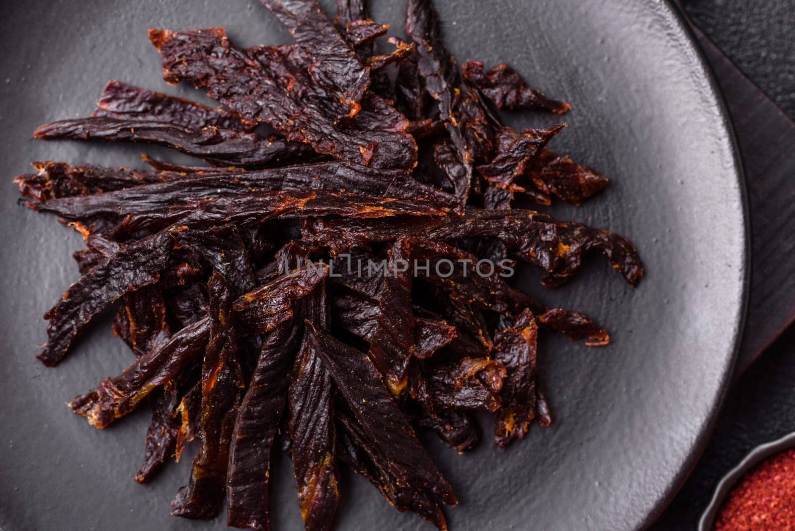 Jerky, dried horse meat or beef slices with salt and spices on a dark concrete background