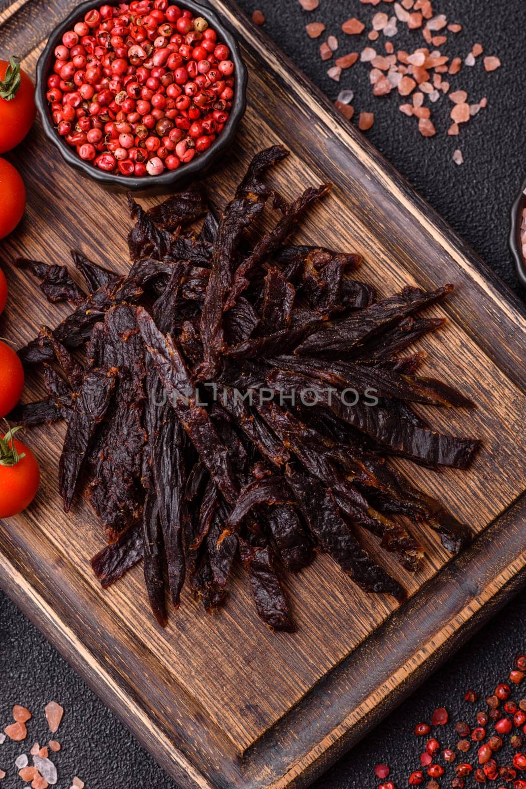 Jerky, dried horse meat or beef slices with salt and spices on a dark concrete background