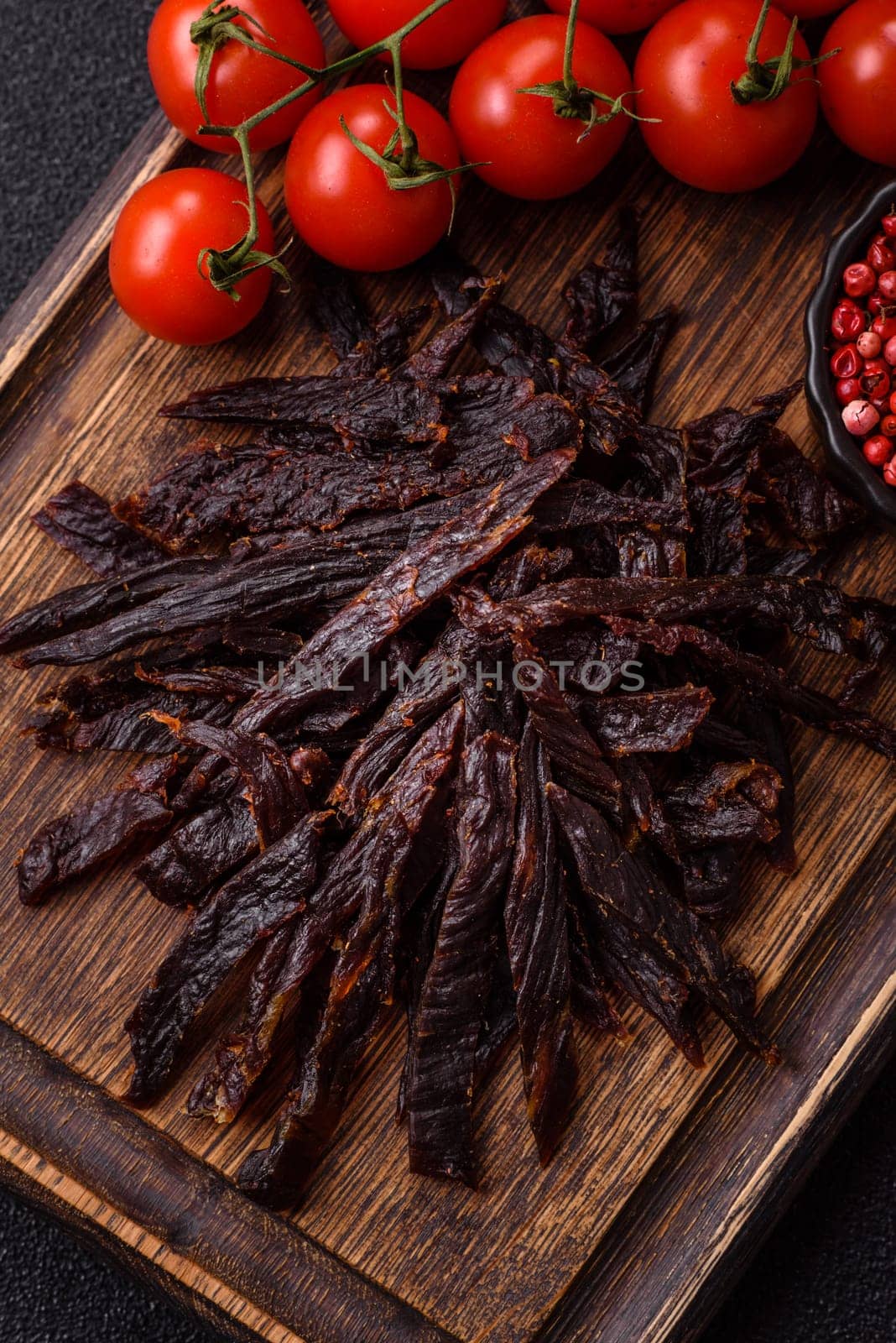 Jerky, dried horse meat or beef slices with salt and spices on a dark concrete background