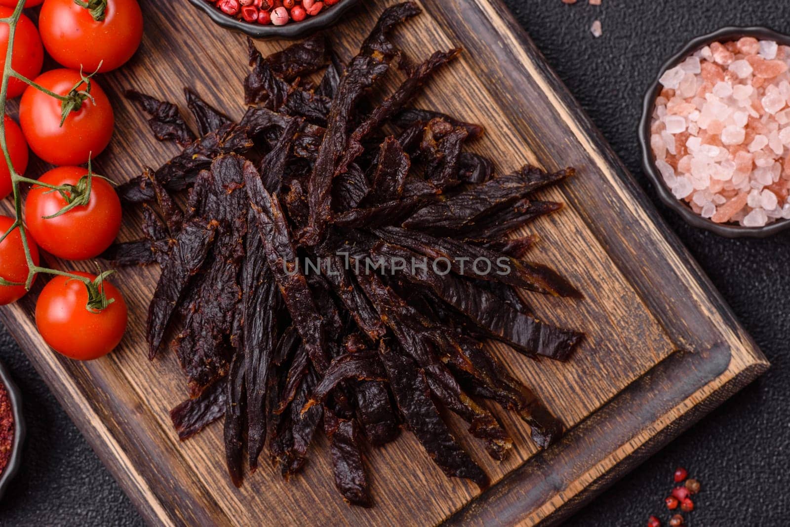 Jerky, dried horse meat or beef slices with salt and spices on a dark concrete background