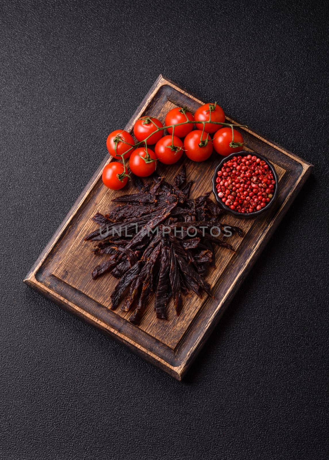 Jerky, dried horse meat or beef slices with salt and spices on a dark concrete background