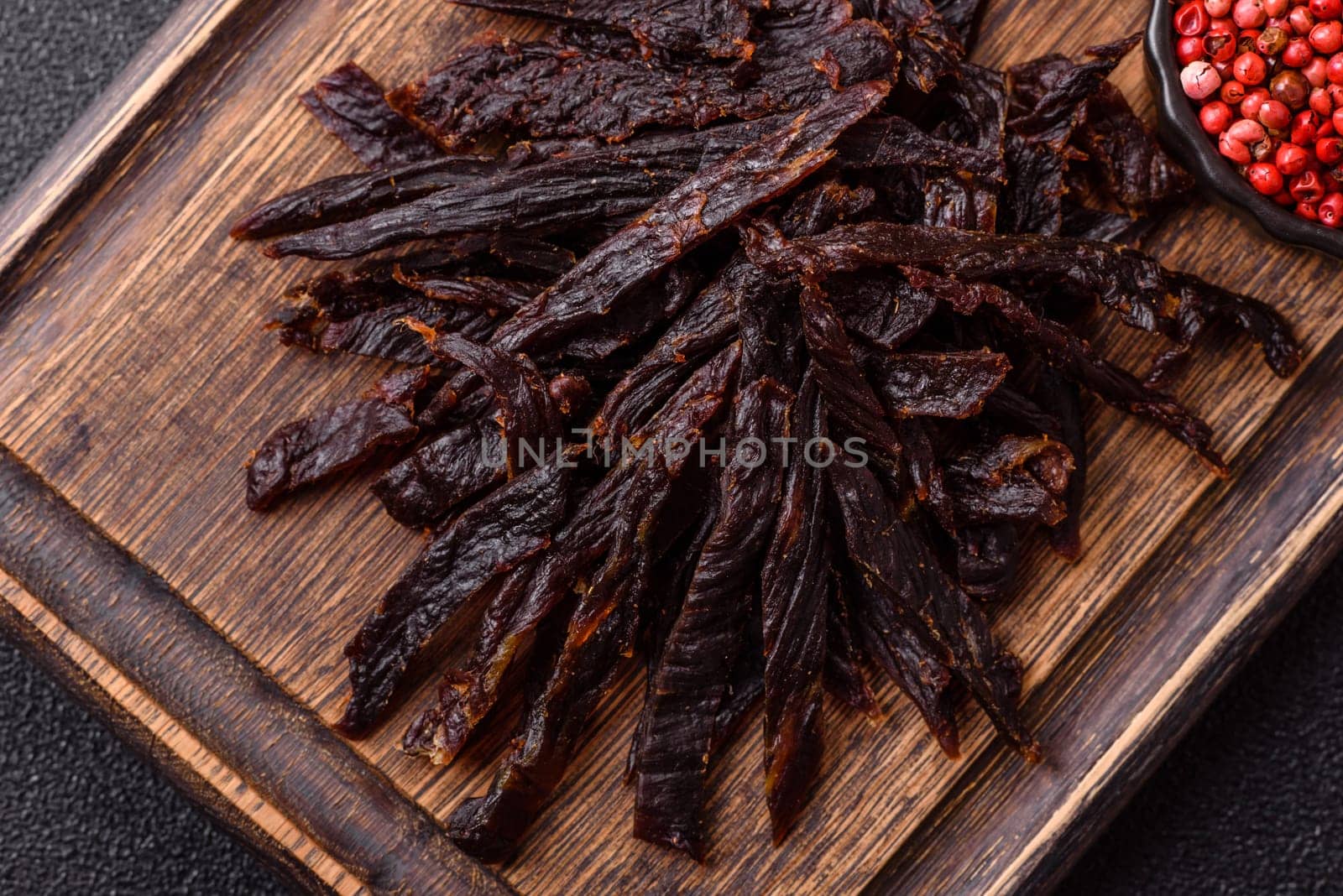 Jerky, dried horse meat or beef slices with salt and spices on a dark concrete background