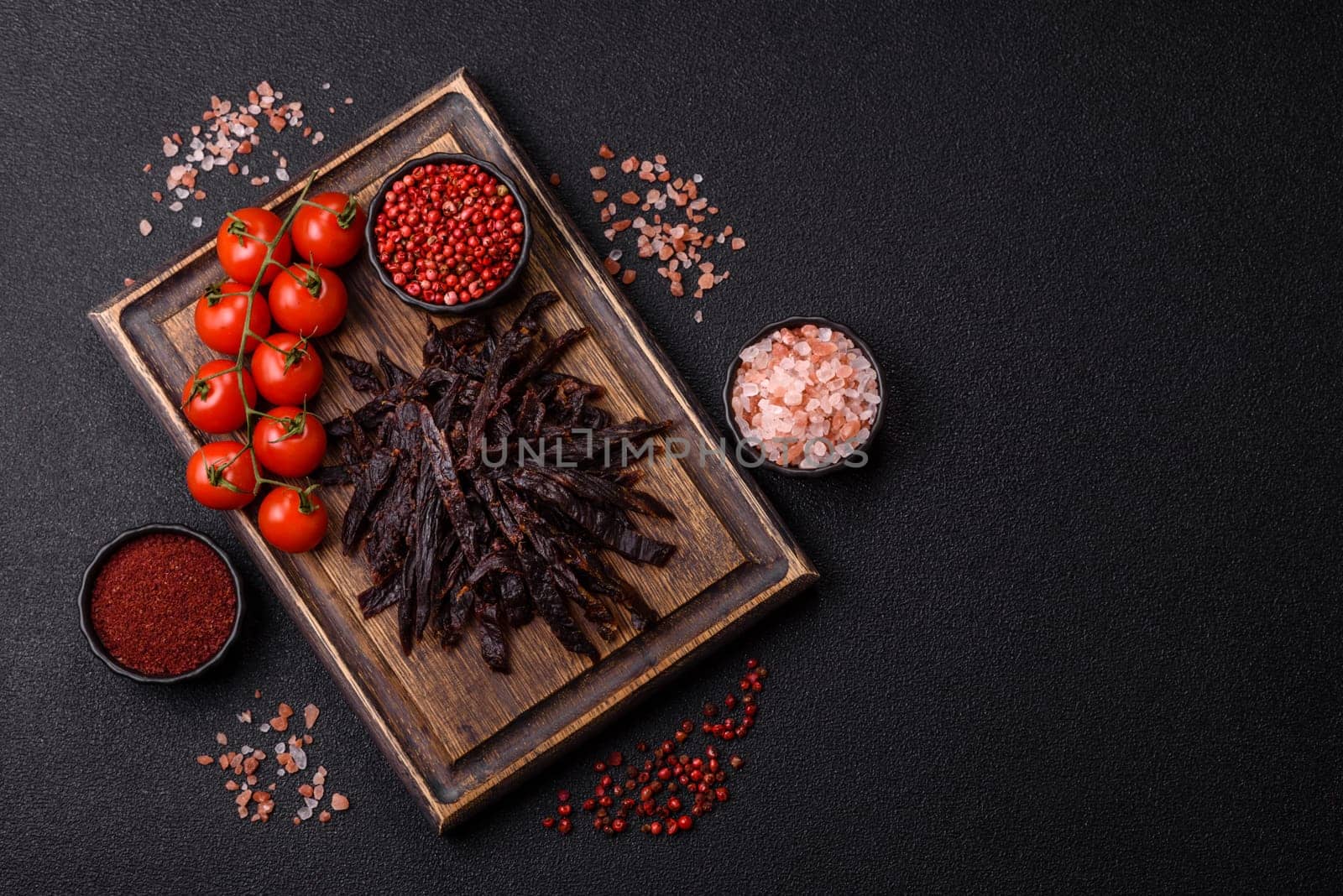 Jerky, dried horse meat or beef slices with salt and spices on a dark concrete background