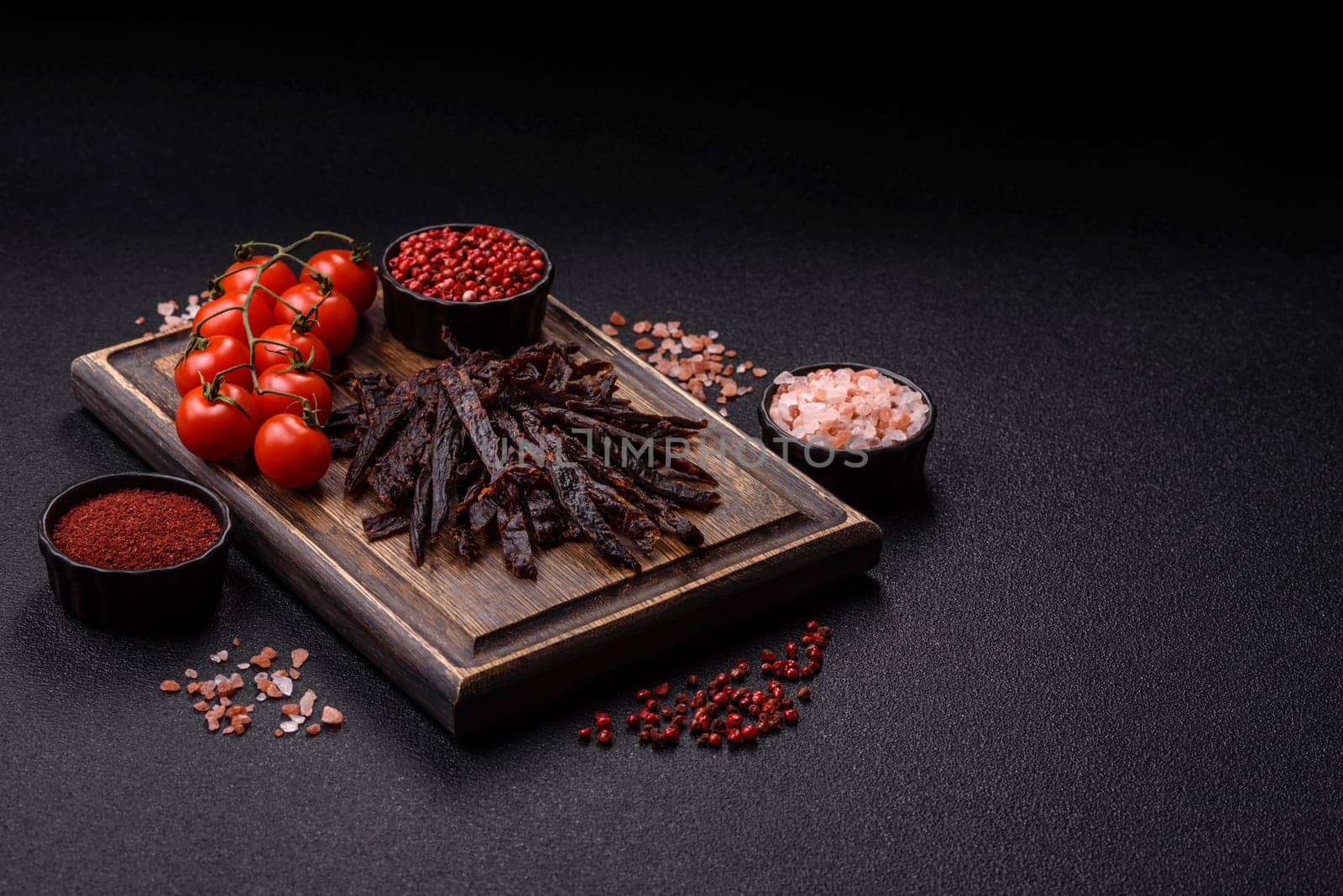 Jerky, dried horse meat or beef slices with salt and spices on a dark concrete background