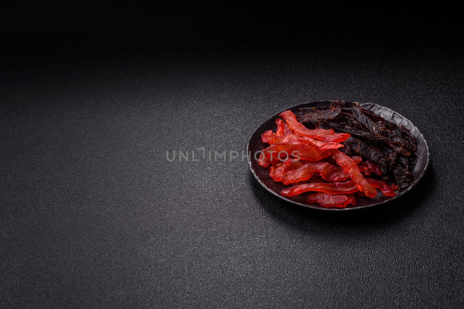 Jerky, dried chicken slices with salt and spices on a dark concrete background