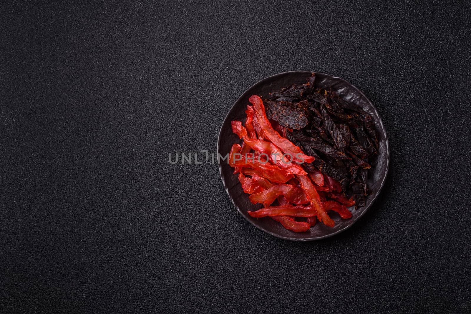 Jerky, dried chicken slices with salt and spices on a dark concrete background