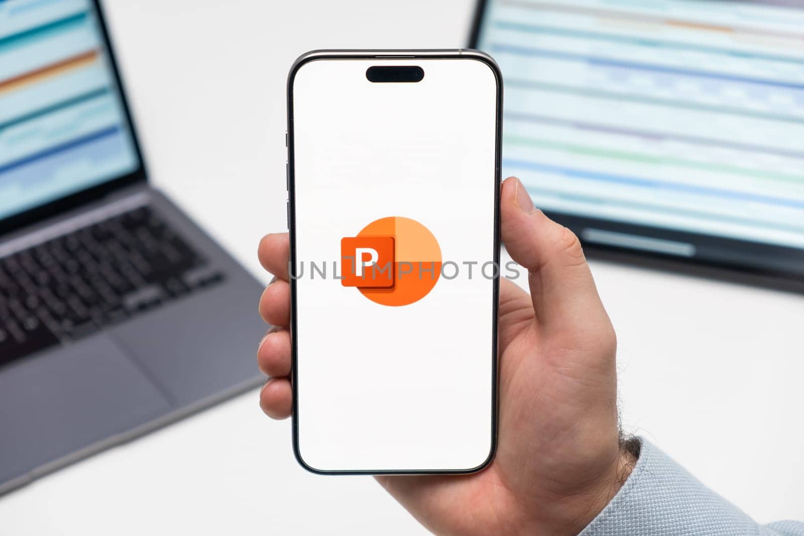 PRAGUE, CZECHIA - JULY, 2024: Power PointPower Point logo on the screen of smartphone in mans hand and laptop on the background
