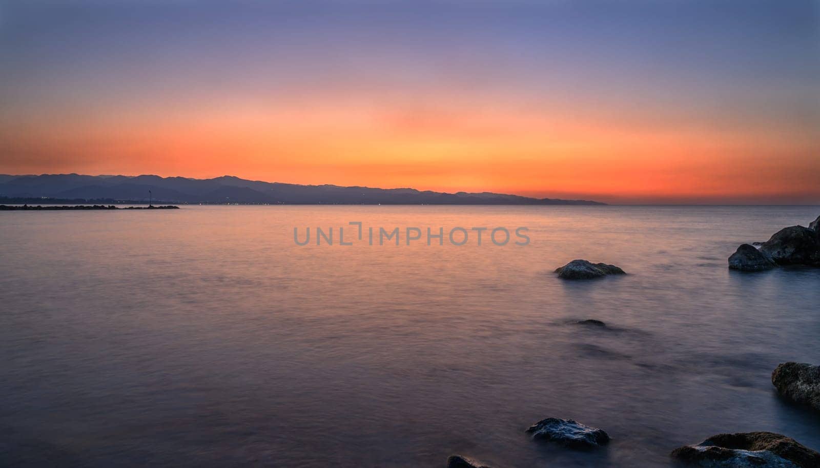Golden and orange rays reflect on tranquil waves as the day comes to a peaceful close near the coastline.