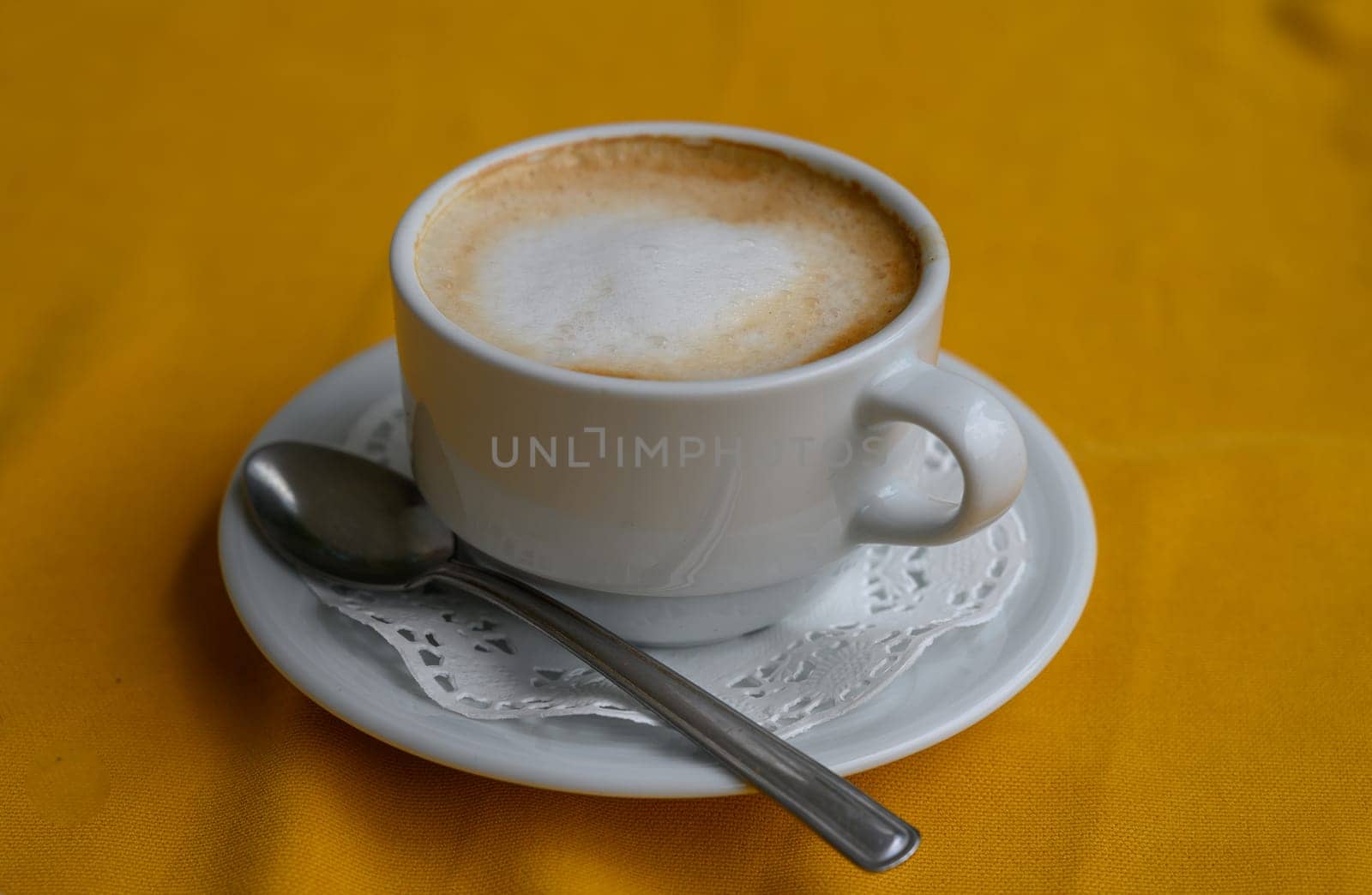 Delicate cup filled with creamy coffee, resting on lace atop a bright yellow surface, inviting warmth and comfort.