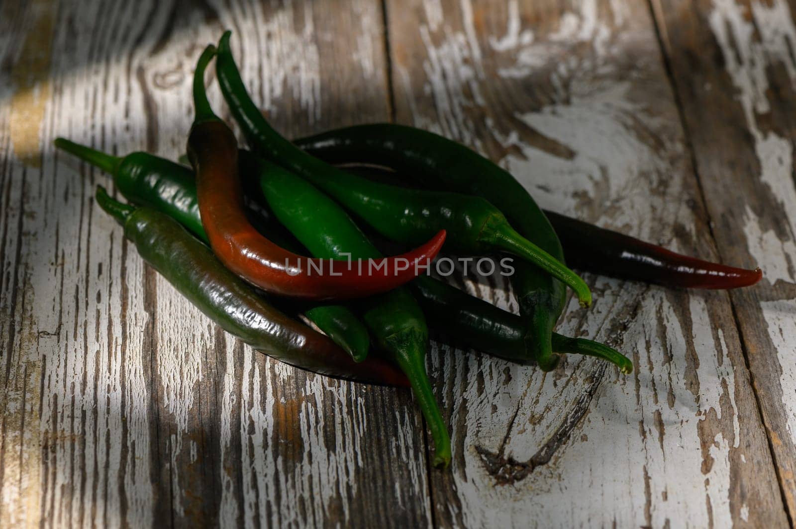 A colorful collection of green and red chilies contrasts beautifully on an aged wooden table, showcasing freshness.