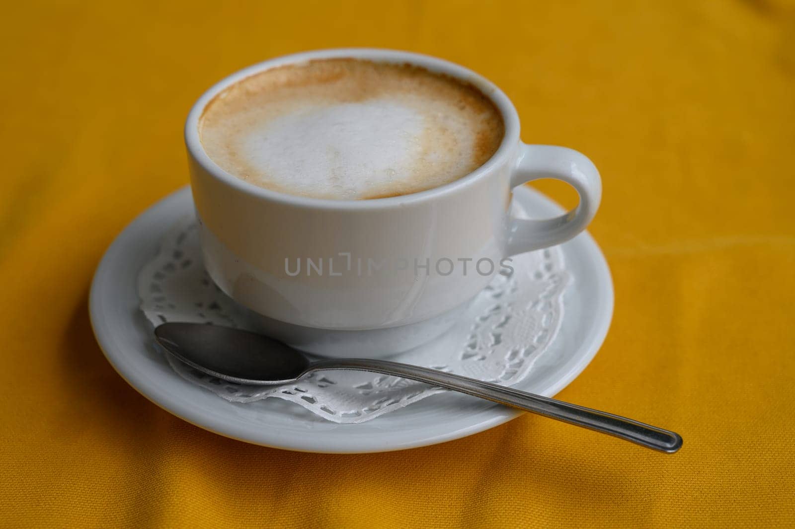 A creamy cappuccino rests on a delicate saucer next to a silver spoon, showcasing warmth and comfort.