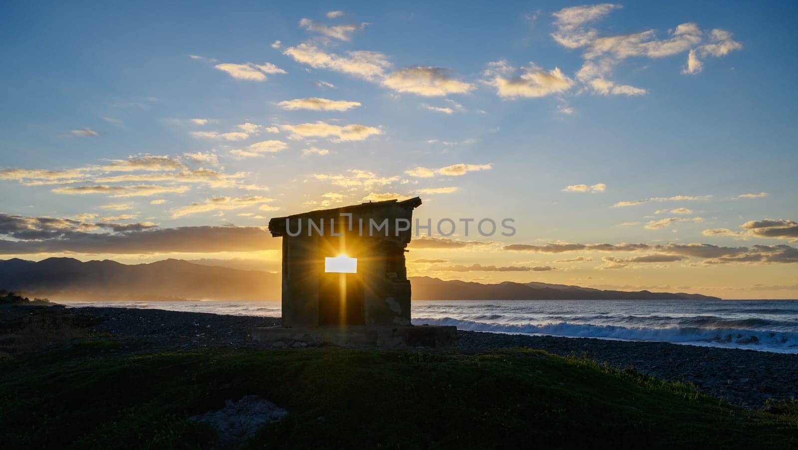 Golden sunlight spills through a crumbling stone wall, highlighting ocean waves at dusk in a picturesque landscape.