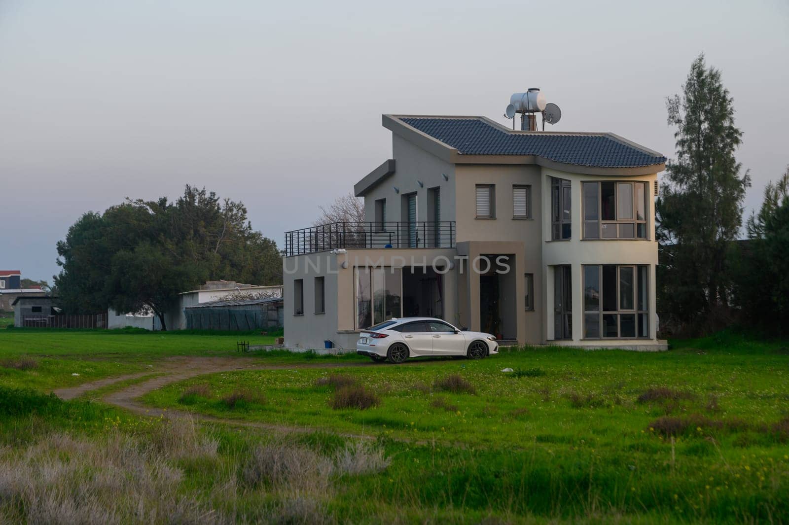 A modern home stands proudly in a vibrant green field, bathed in the soft light of evening, evoking tranquility.