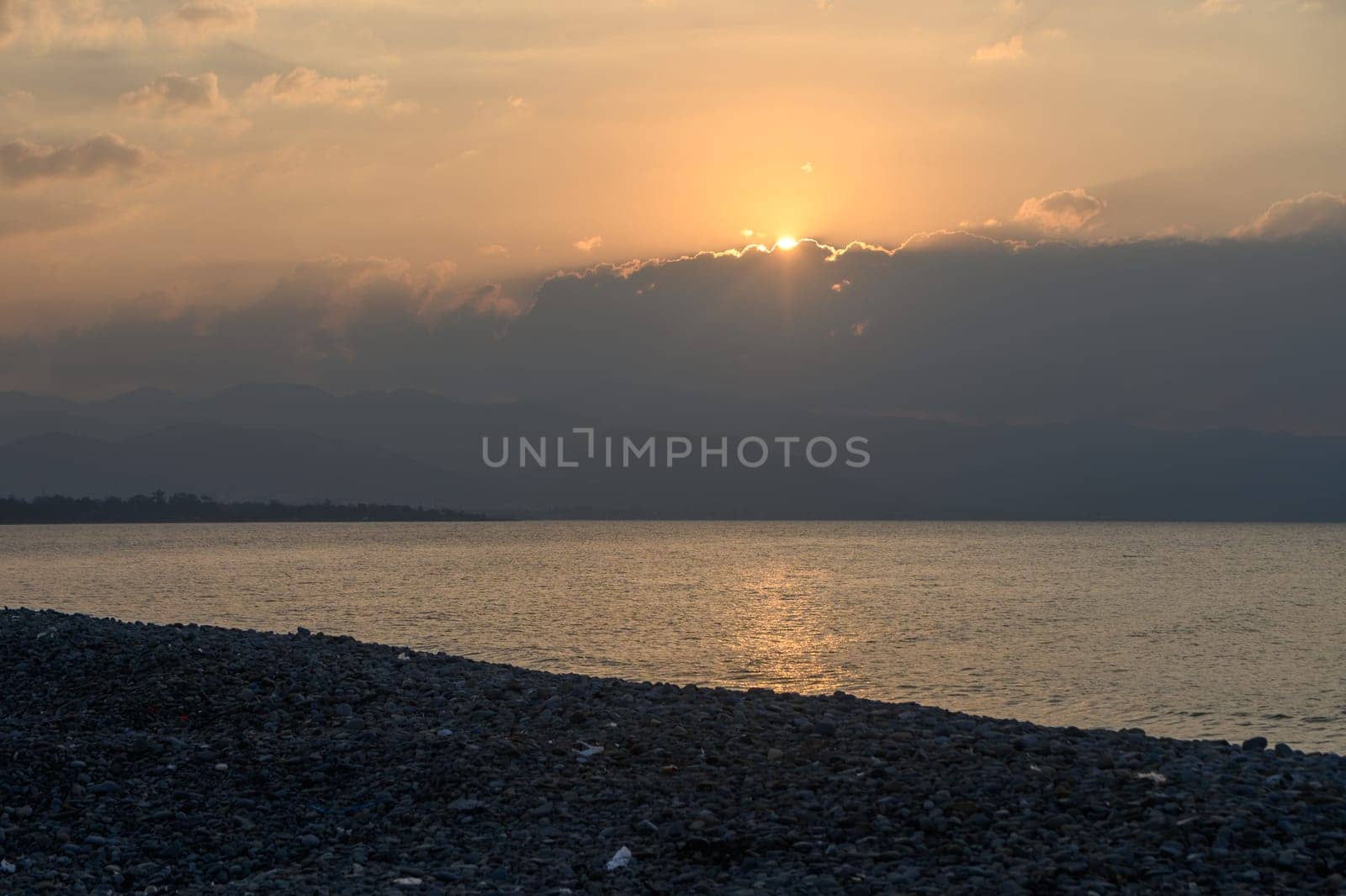 Golden rays break through clouds, illuminating the calm waters and rocky shoreline during a peaceful evening.