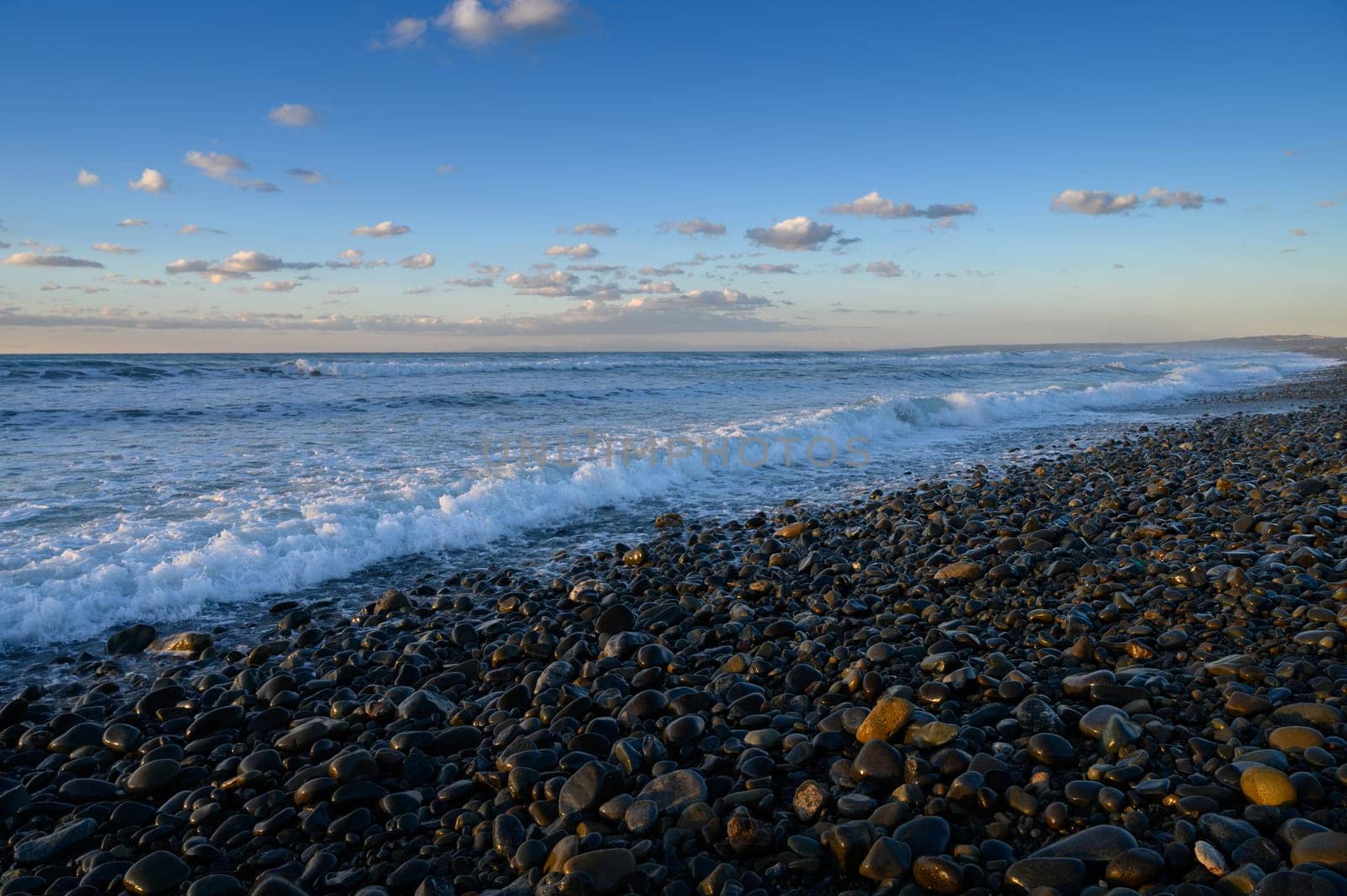 Waves gently crash on a rocky beach while clouds drift across a vibrant sky during the beautiful evening light.