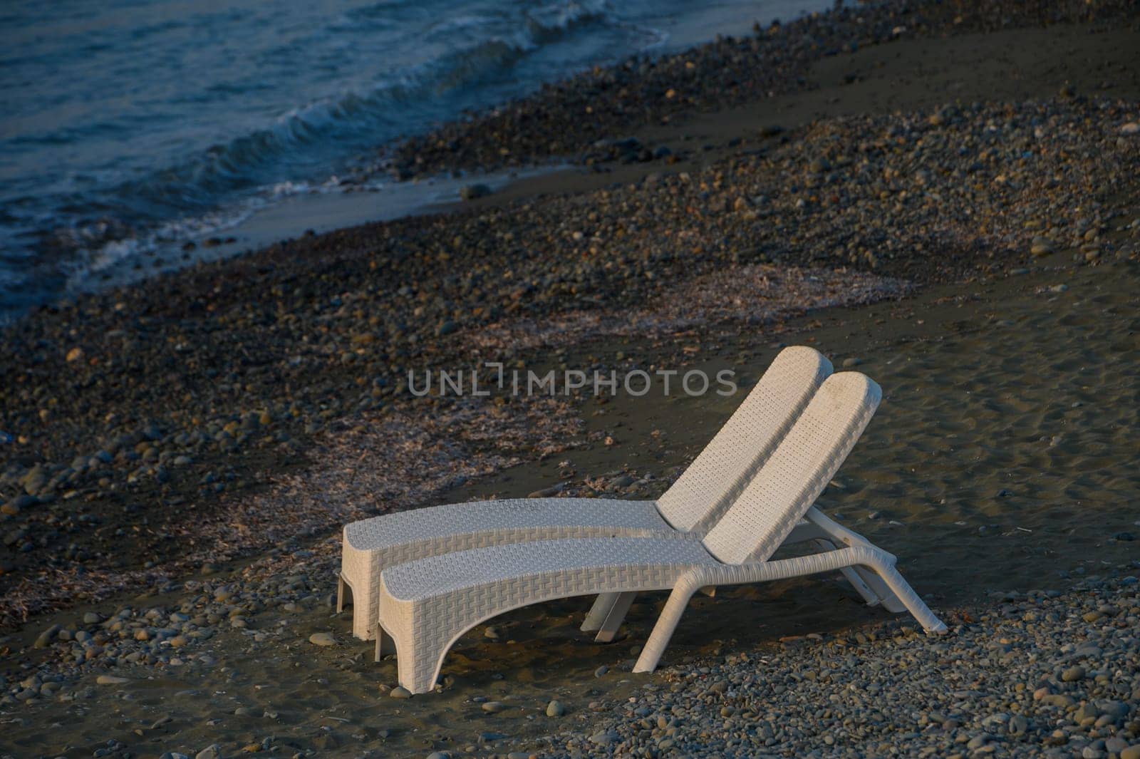 Two white loungers sit peacefully on the shore, overlooking gentle waves at dusk, inviting quiet reflection and calm.