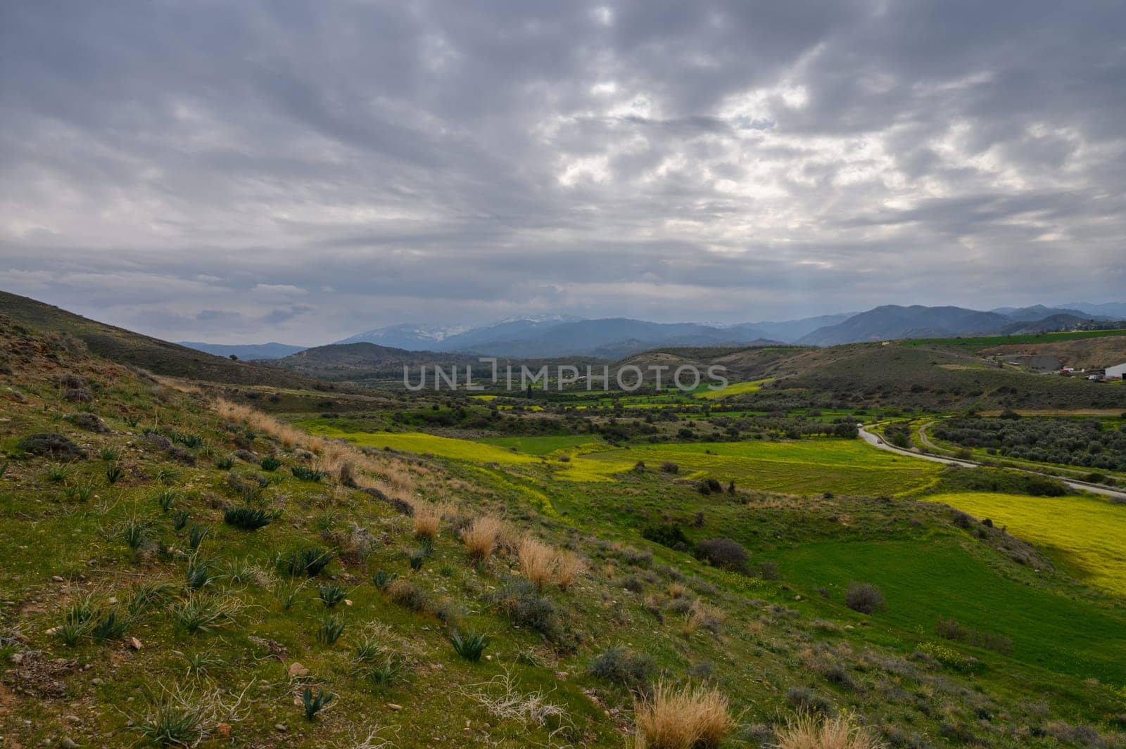 Lush green fields stretch across the valley as storm clouds gather overhead in a tranquil countryside panorama.