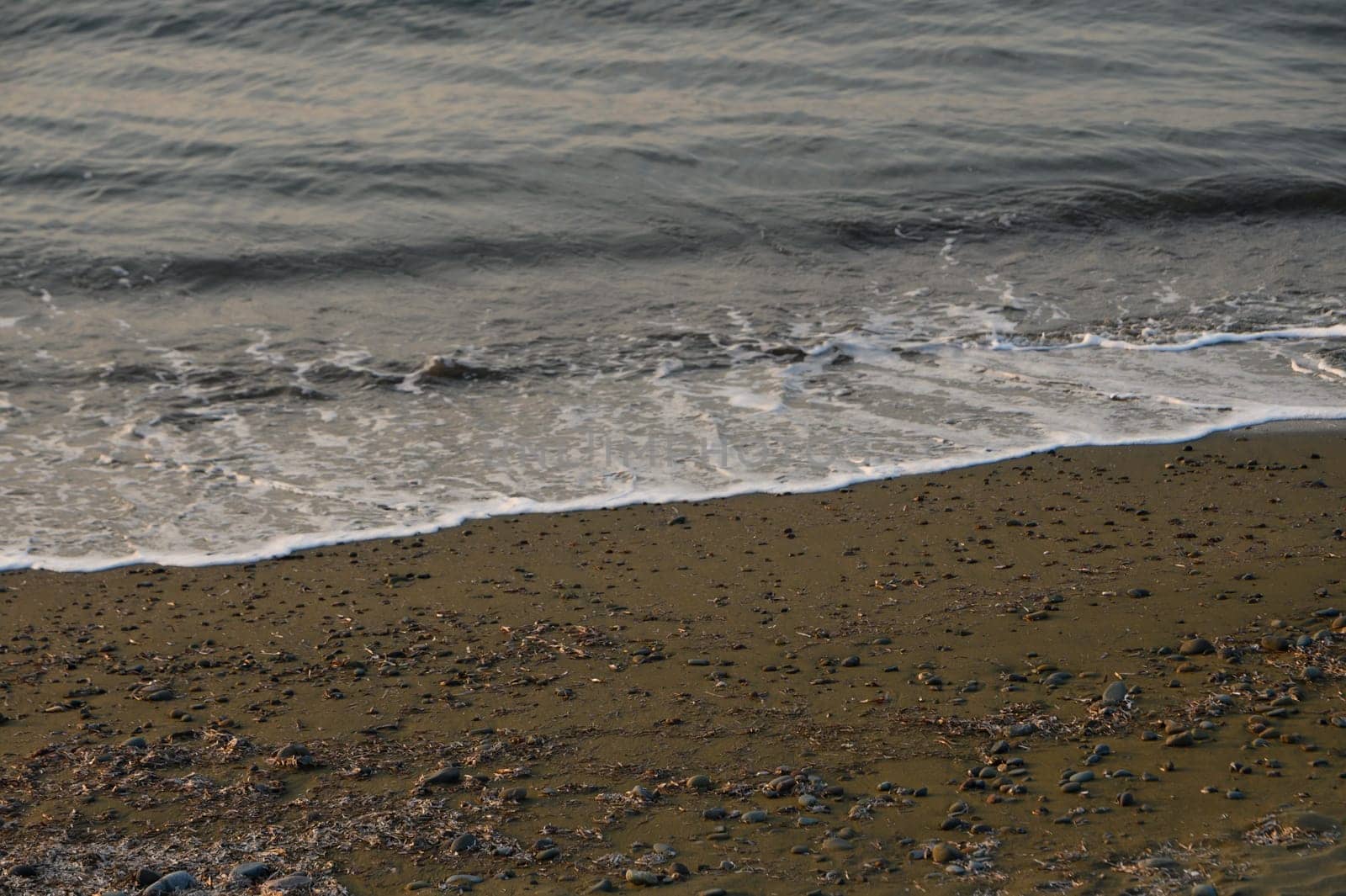 Soft waves roll onto a stony beach as dusk descends, casting a serene atmosphere by the water's edge.