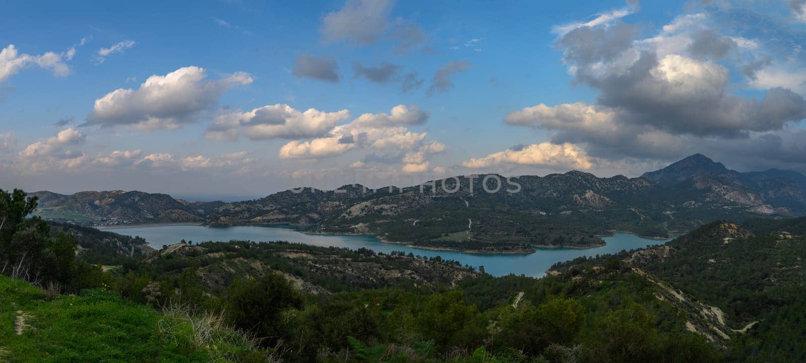 Calm waters reflect the changing colors of the sky as clouds drift peacefully over lush hills at dusk.