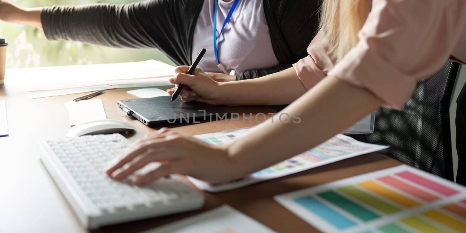 Close-up of two female graphic designers using digital tools and color palettes, highlighting teamwork and creativity in a modern office environment.