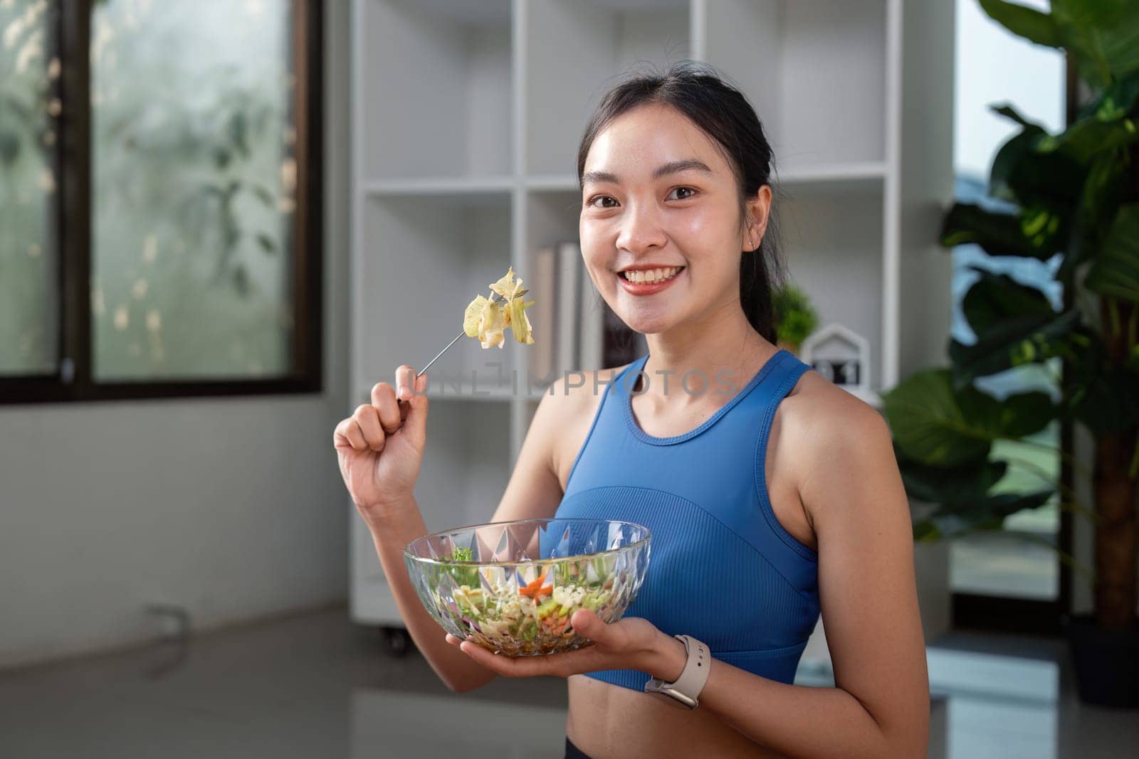 A happy woman in sportswear enjoying a colorful salad in a modern kitchen, emphasizing a healthy lifestyle and nutrition.