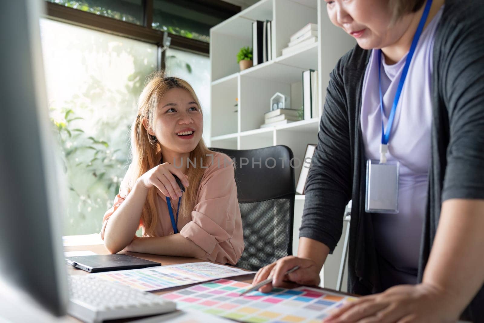 Two female graphic designers smiling and discussing color palettes, emphasizing teamwork and creativity in a modern workspace filled with natural light.